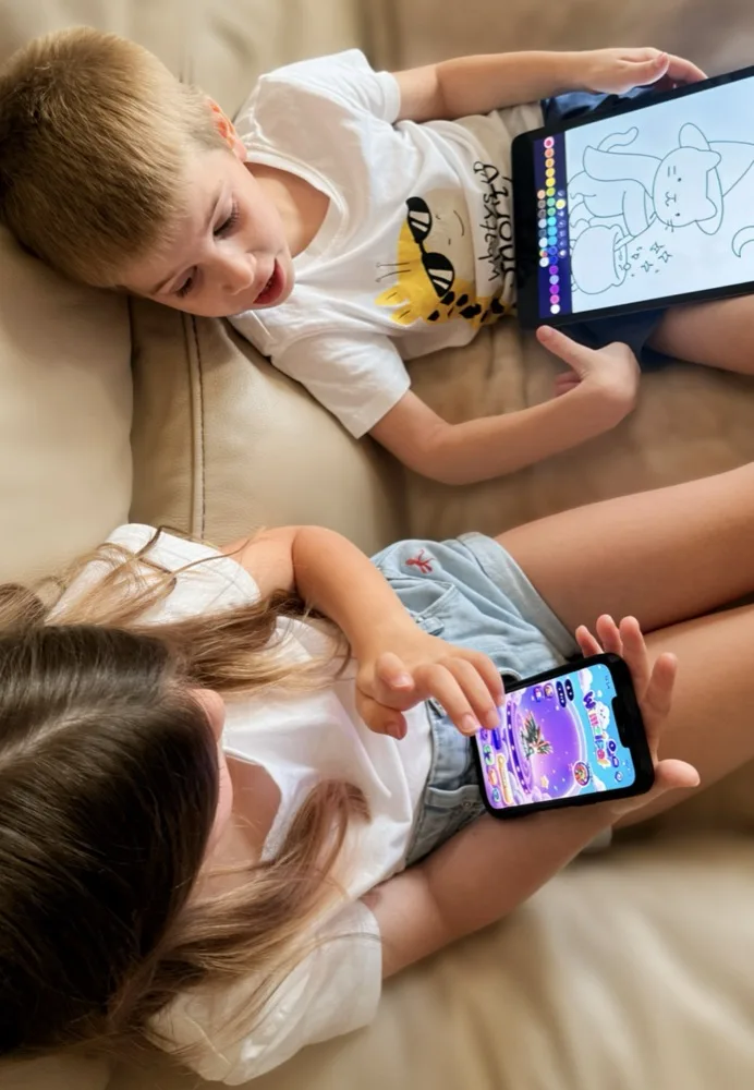 The founder's two young nephews side by side on a couch, one coloring a puppy in WimziPal on an iPad, the other playing WimziPal on a phone